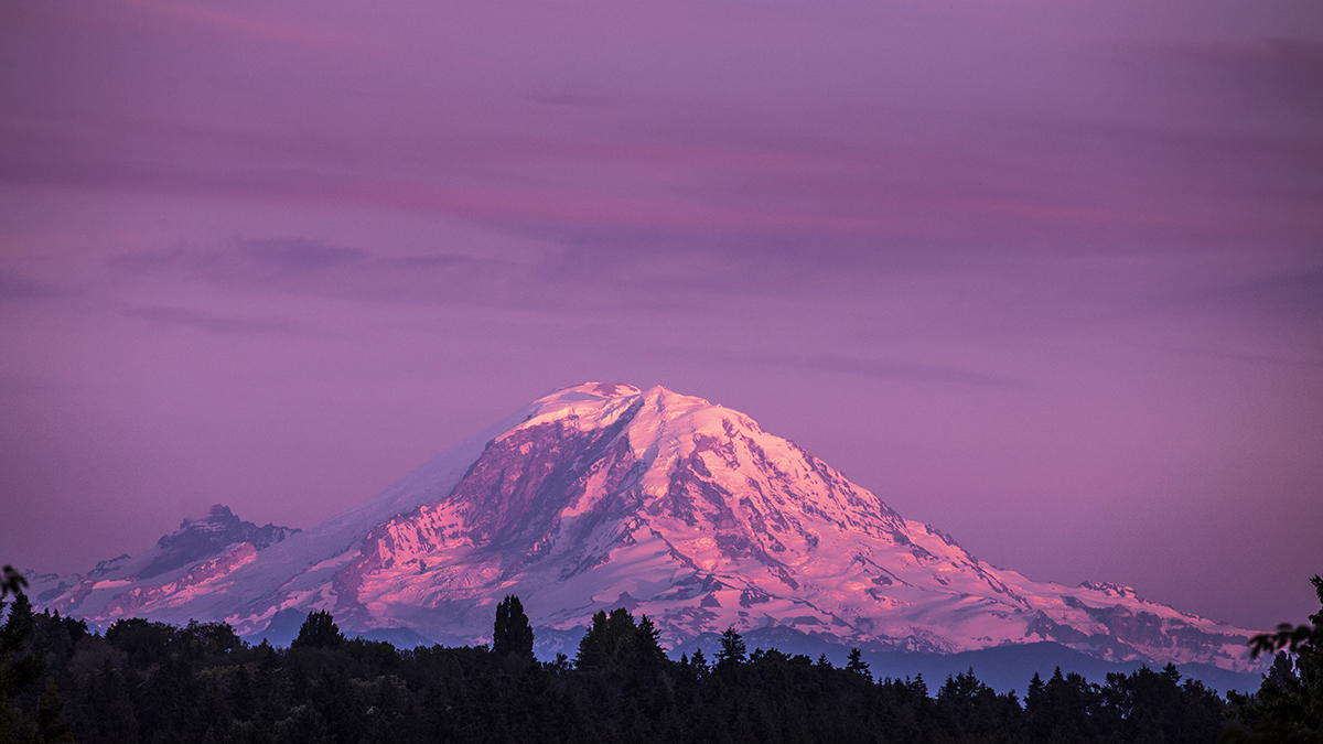 A snow-capped Mount Rainer in silhouette against a purple sky.  
