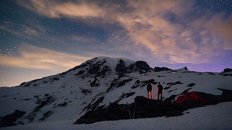 Two people are standing on a PNW mountain, lookin up at the starry sky. Photo credit: Soren Johnson.