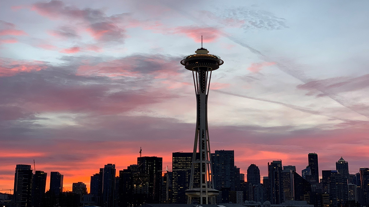 A view of the Space Needle and downtown skyscrapers in silhouette against a red and purple sunrise. 